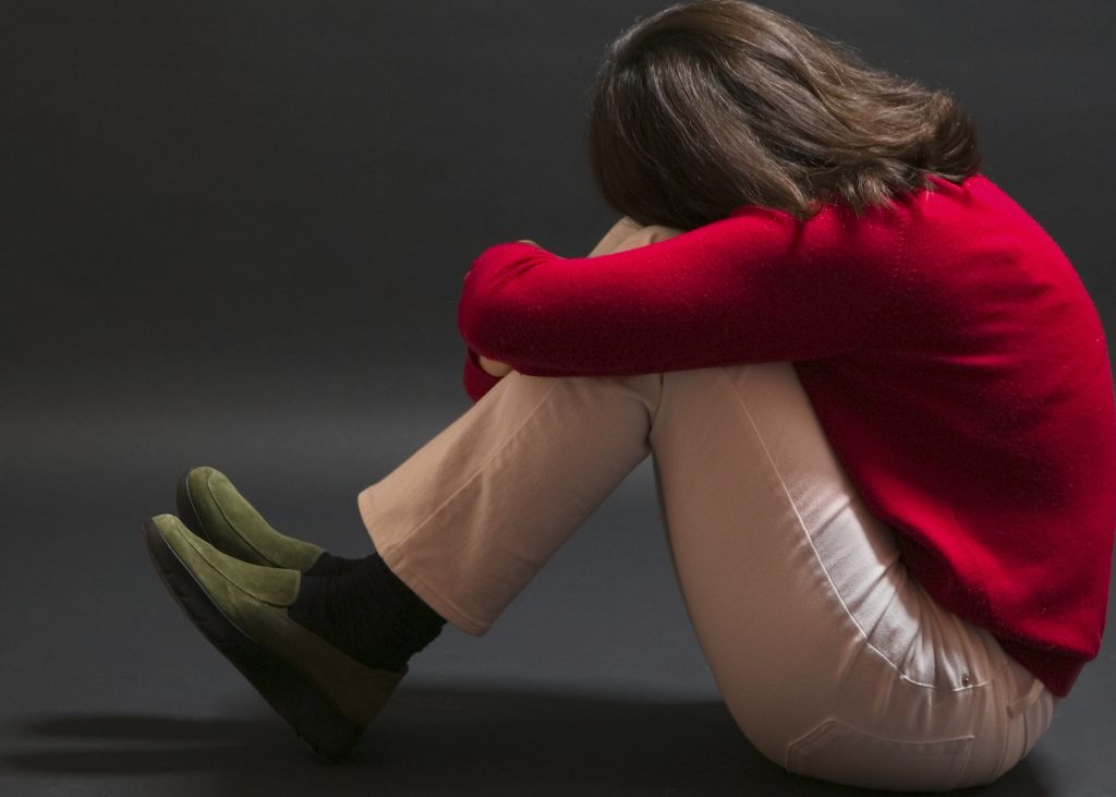 Woman pulling knees in and looking away. Pose, combined with dark background and tight framing suggest feelings of stress or being limited and without options.